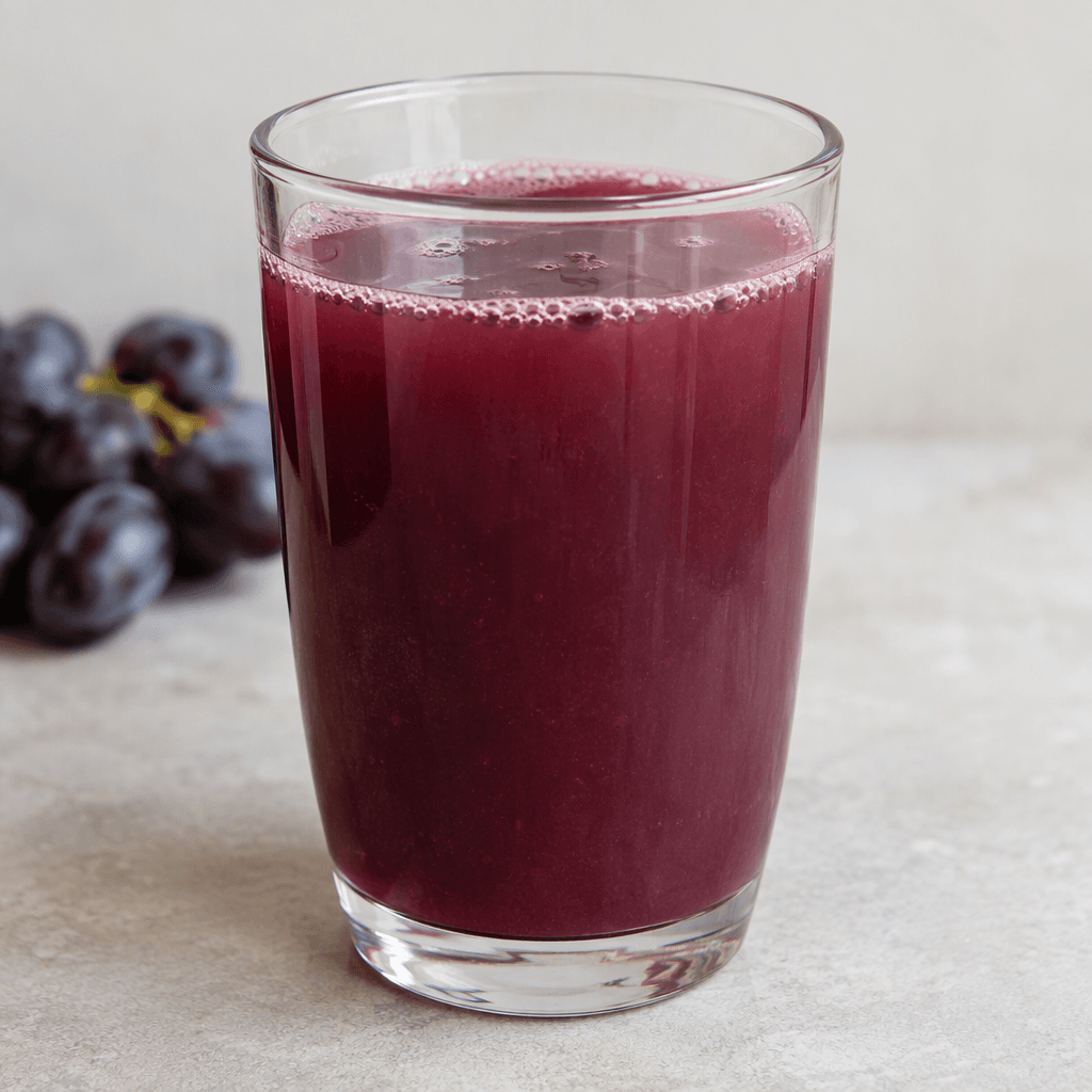 Deep purple-red grape juice with a slightly cloudy, translucent appearance fills a clear drinking glass, with a few small bubbles visible near the surface.