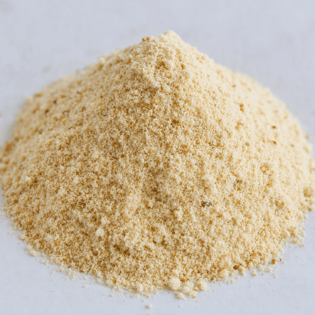 A mound of fine, pale beige powder with tiny darker biscuit-colored flecks, loosely piled on a clean surface.