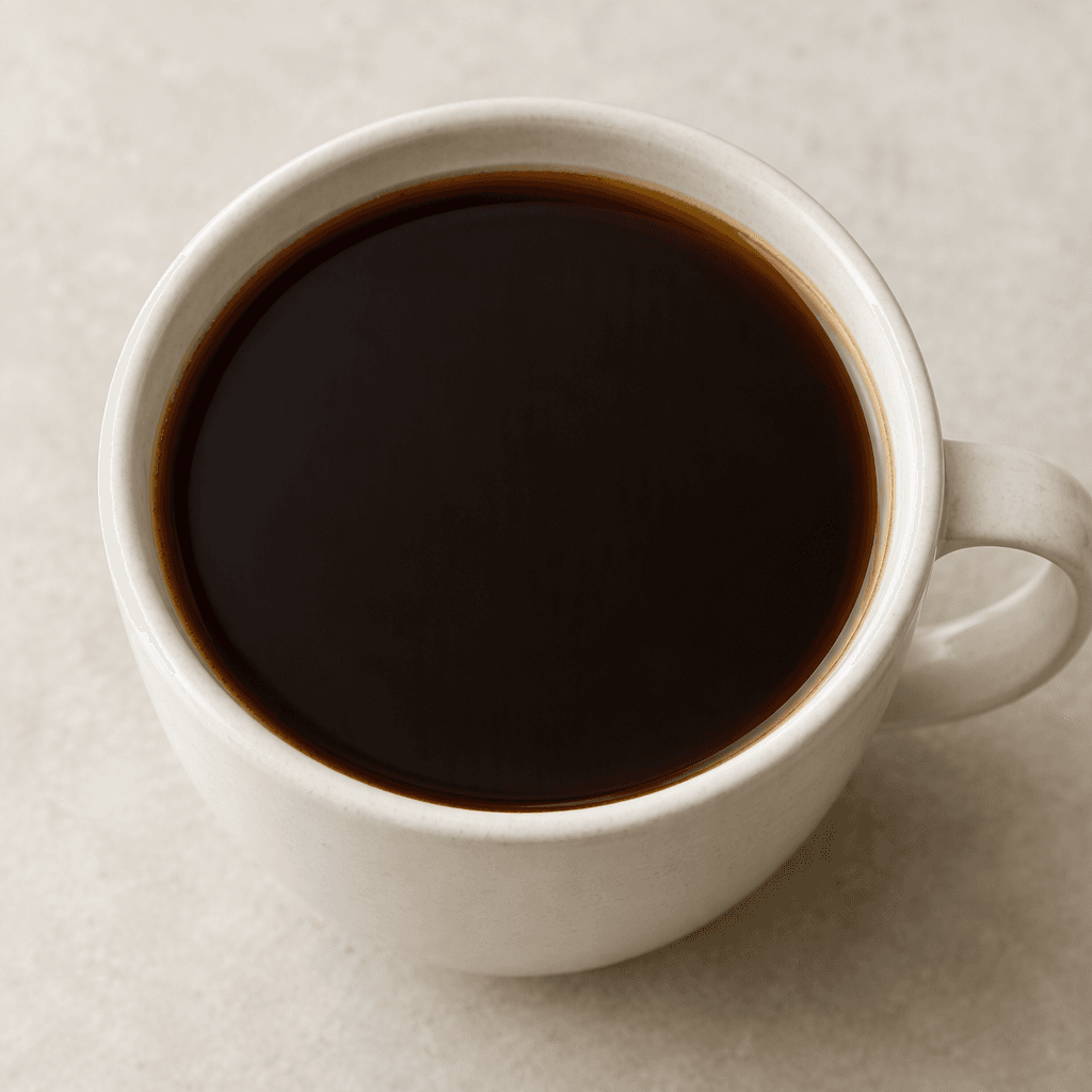 Dark brown, nearly opaque coffee fills a simple cup, with a smooth surface and a slightly lighter brown edge where the liquid meets the rim.
