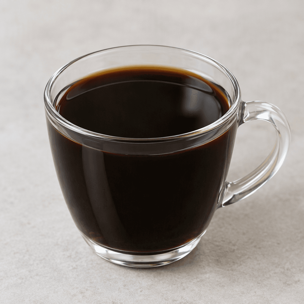 A clear glass cup filled with very dark brown, almost black coffee, its smooth surface showing a faint reflective sheen and no sugar, milk, foam, or visible sediment.