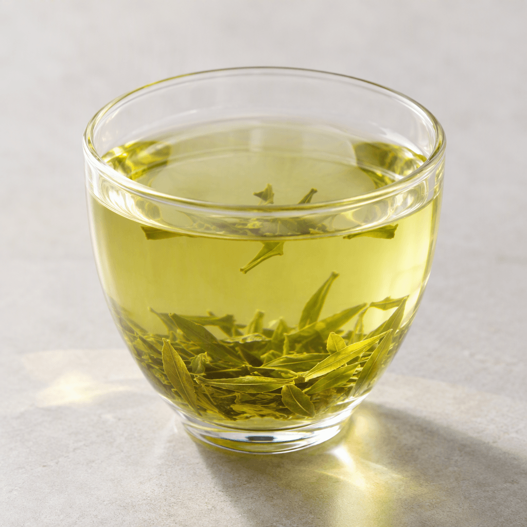 A clear, pale golden-green tea drink sits in a glass, with light catching its translucent surface.