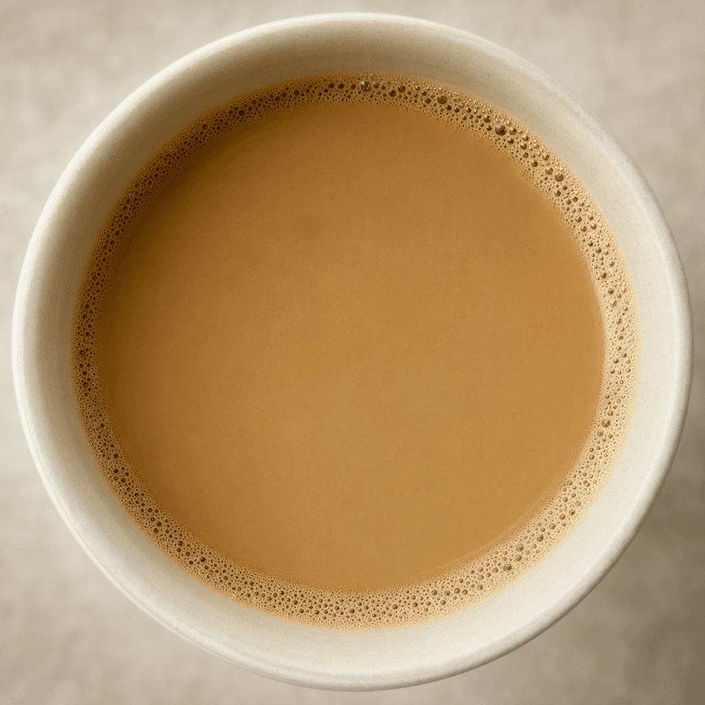 A smooth, medium-brown instant coffee fills a plain cup, with a light tan surface and a thin ring of fine bubbles around the edge.