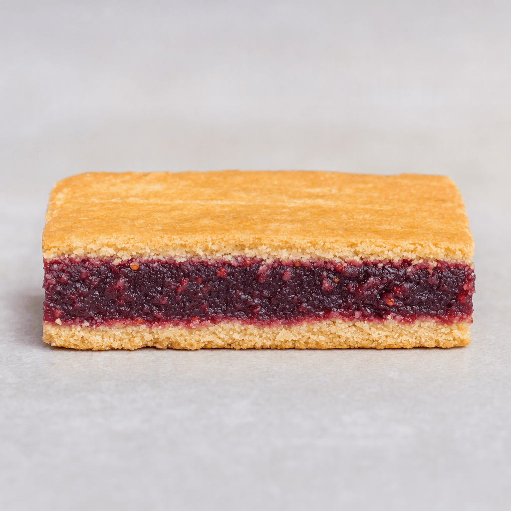 A slim rectangular fruit bar with a deep red-purple filling visible between two thin, pale golden-brown biscuit layers, its cut edges showing a slightly crumbly texture.