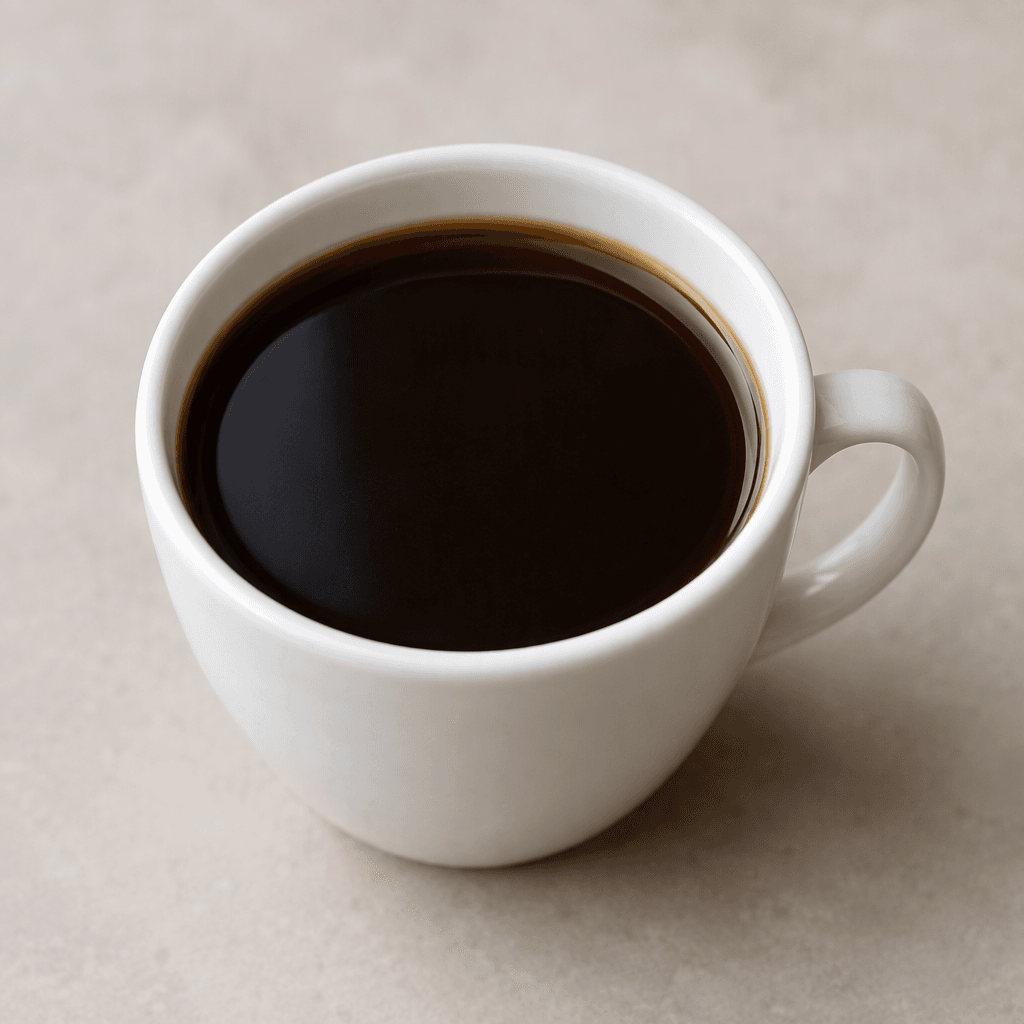 A small cup filled with opaque, very dark brown coffee, its smooth surface showing a faint sheen and no milk or foam.