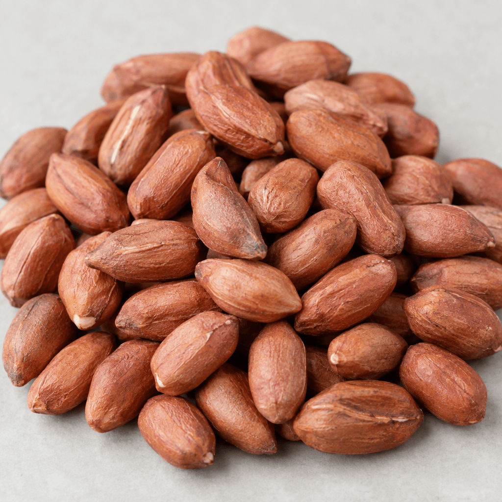 Oblong peanut kernels with thin reddish-brown skins and a lightly wrinkled surface are piled loosely together.