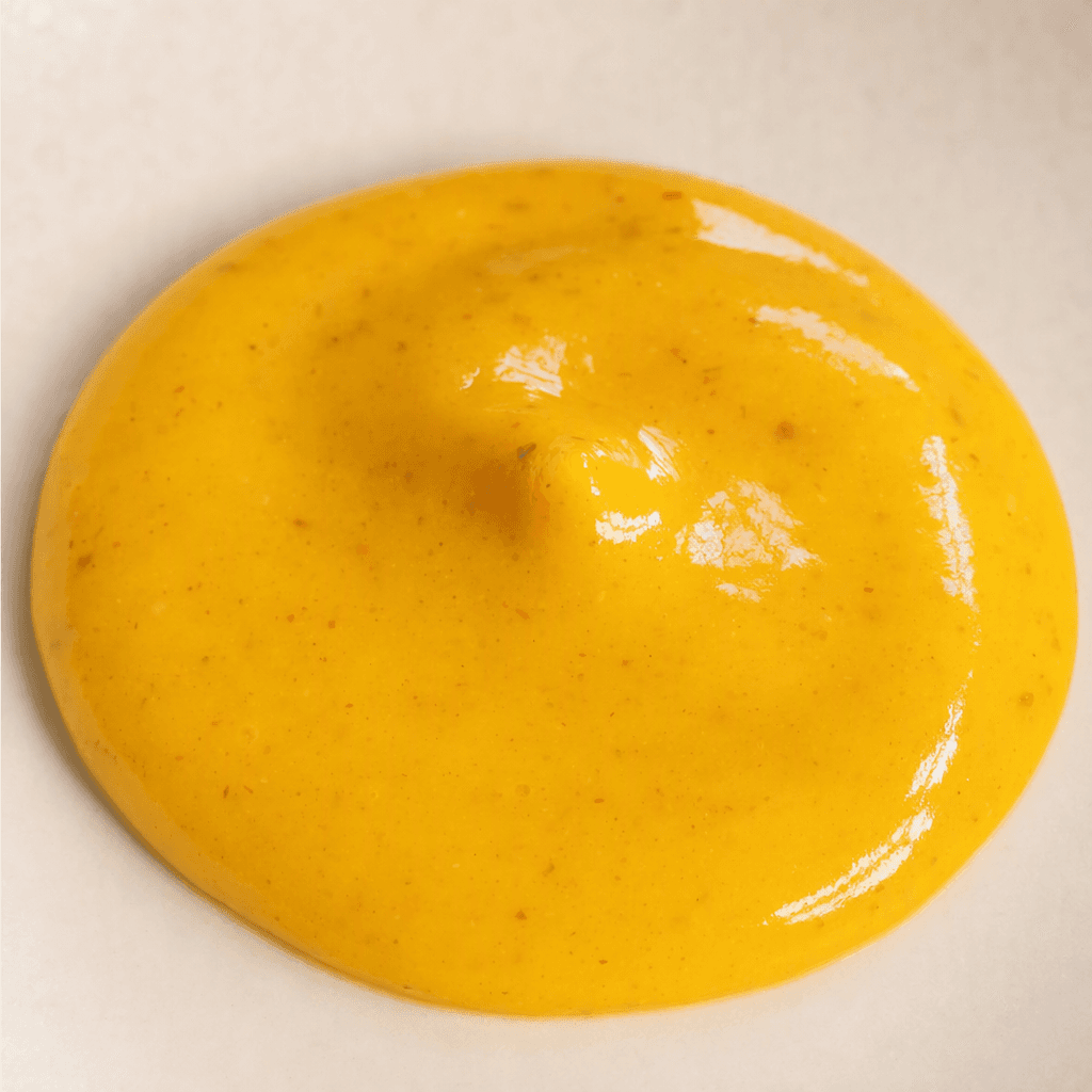 A glossy, thick golden-yellow hot sauce with a smooth, slightly speckled surface sits in a small pool.