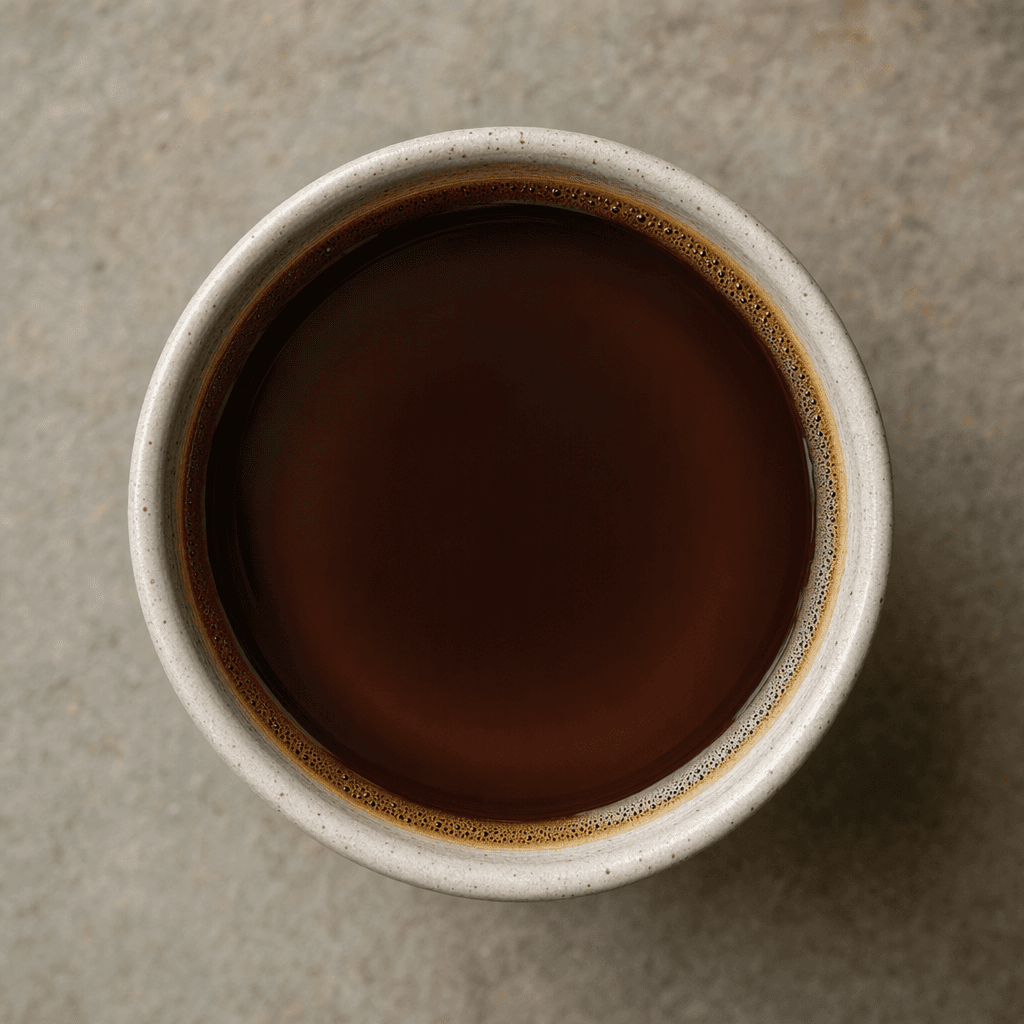 A dark brown coffee fills a small cup, with a smooth surface and a thin tan ring around the edge.