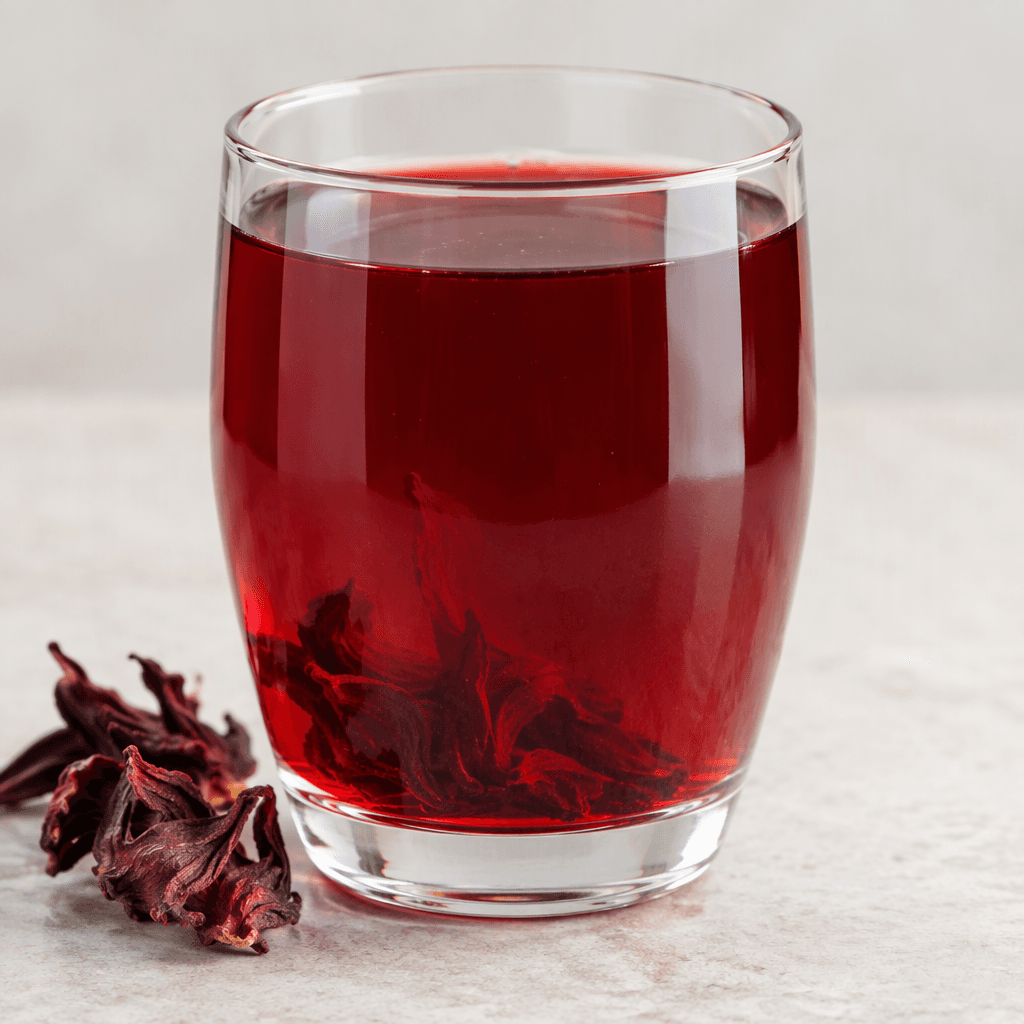 A clear, deep ruby-red hibiscus drink fills a transparent glass, its surface catching the light.