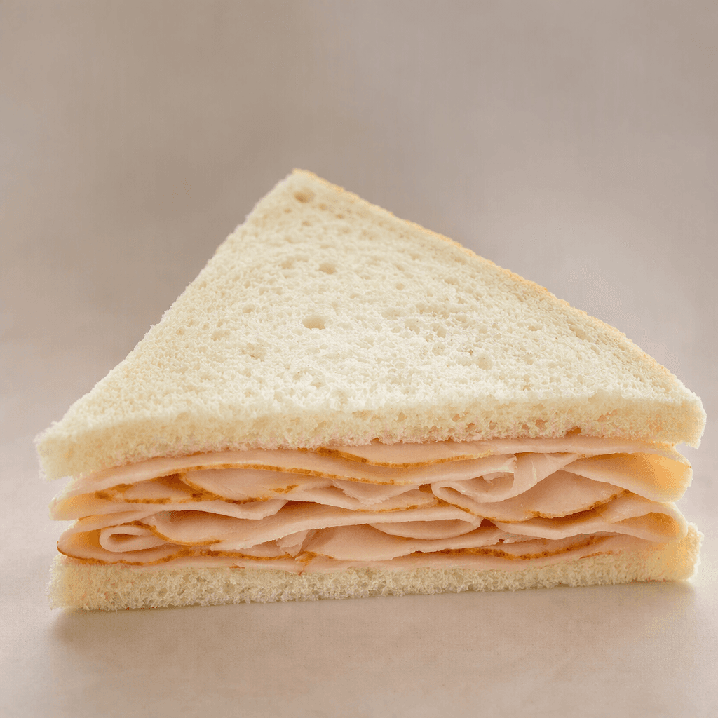 A triangular sandwich made with two slices of soft white bread, filled with thin pinkish-brown smoked turkey slices and cut diagonally to show the layered filling.