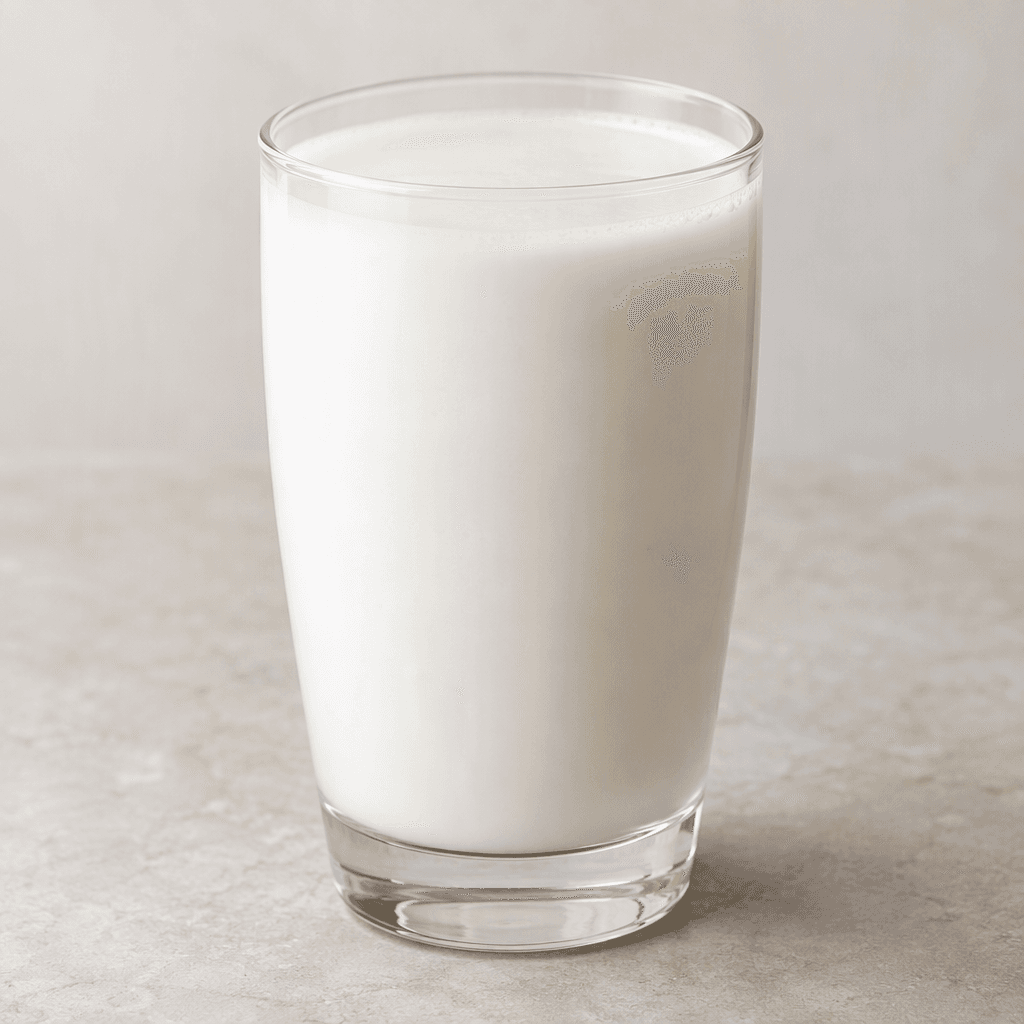 A smooth, opaque off-white coconut-based drink fills a clear glass, with a lightly creamy surface and no visible pieces.