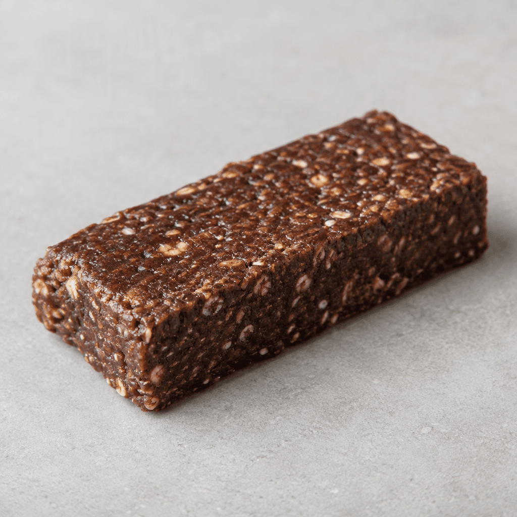 A single rectangular chocolate protein bar with a dark brown, slightly rough surface and visible lighter flecks, resting on a plain surface.