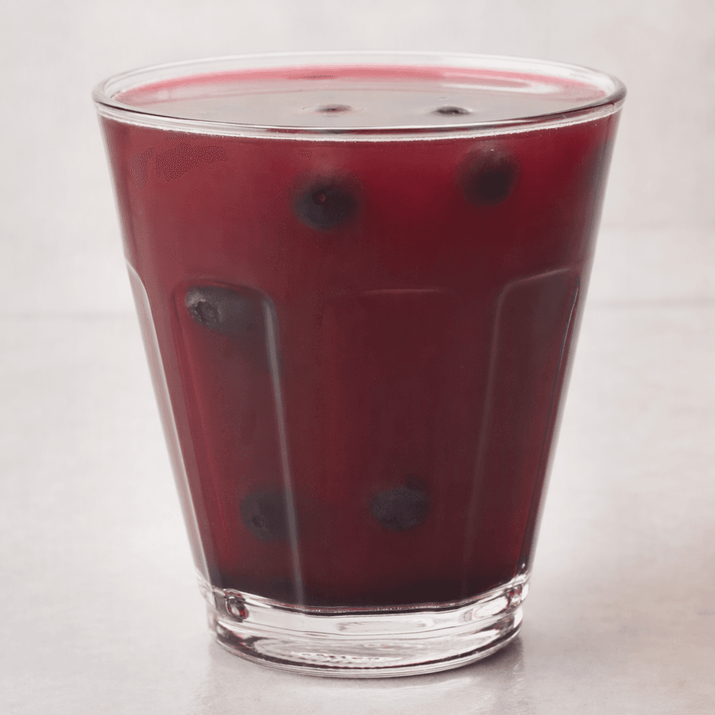 A deep purple-red, slightly translucent drink fills a clear glass, with a smooth surface and a few dark berries visible inside.
