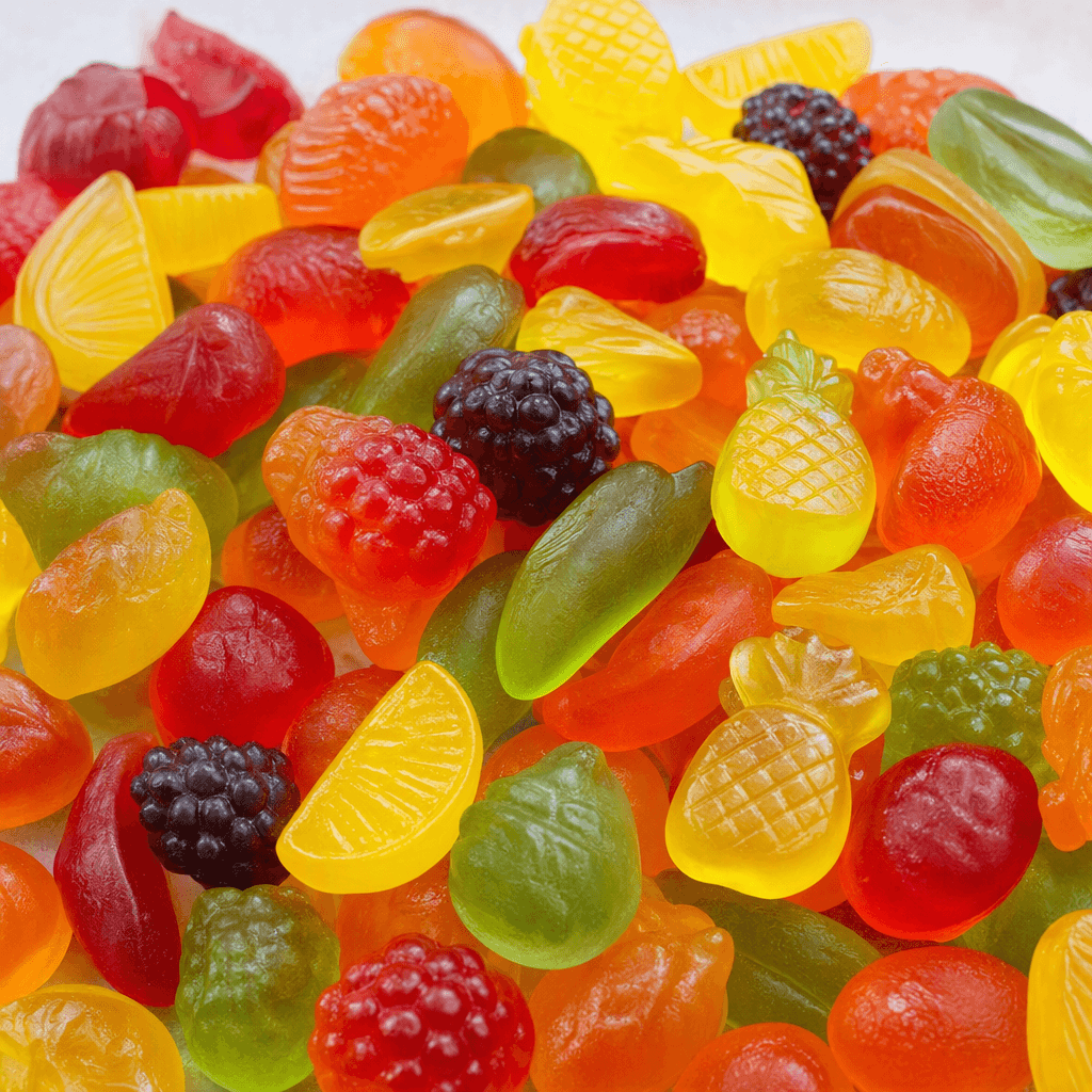 Small, glossy, translucent fruit gummies in assorted bright colours and playful shapes are scattered together.