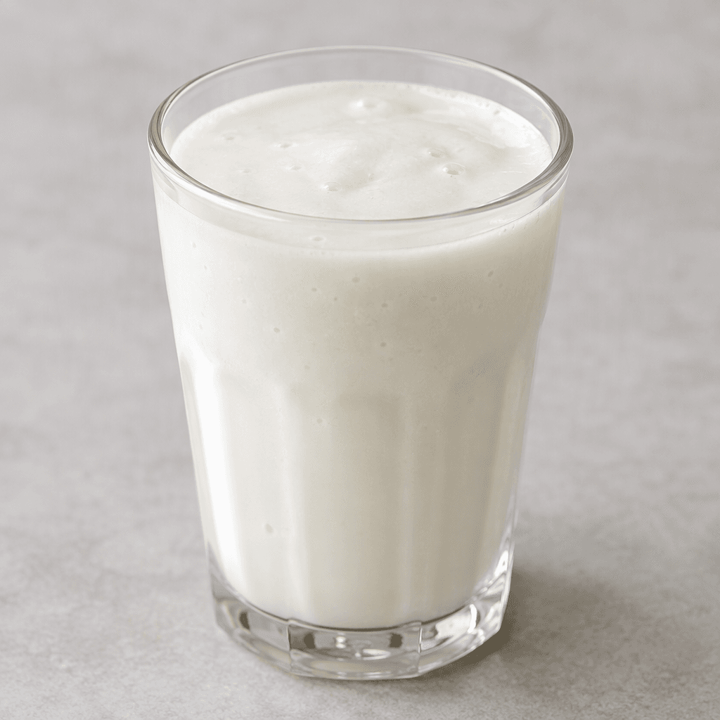 An opaque milky-white drink with a smooth, slightly thick texture and a few tiny bubbles, served in a clear glass.