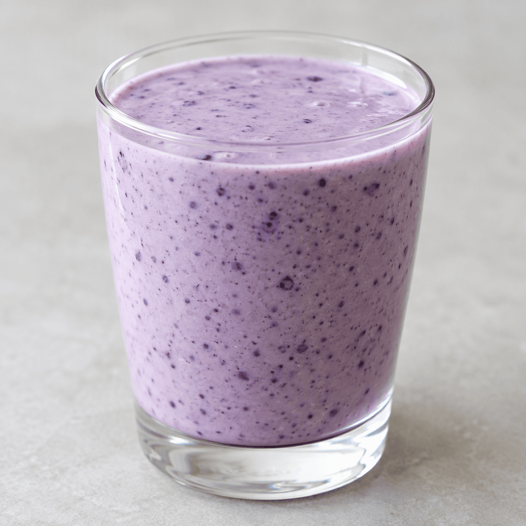 A creamy, pourable lavender-purple kefir with fine darker berry flecks, served in a clear glass.