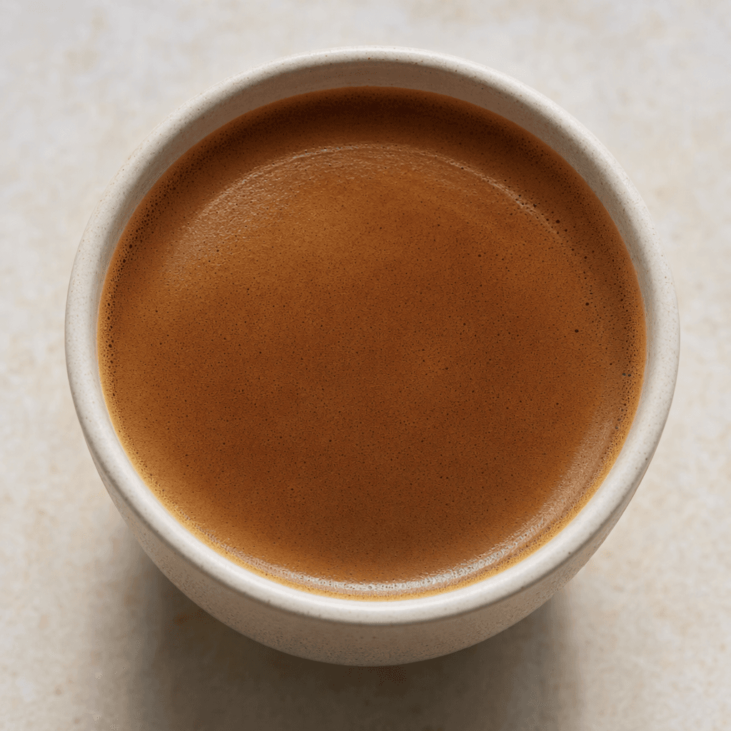 A smooth, deep-brown coffee served in a plain cup, with a lightly foamy surface.