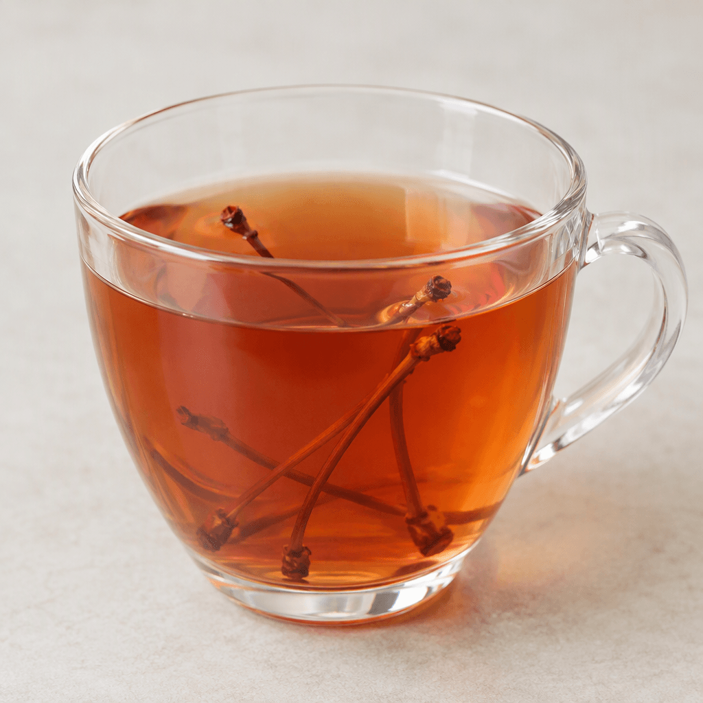 A clear cup holds a pale amber-red herbal infusion, with a few thin, reddish-brown cherry stems visible in the liquid.