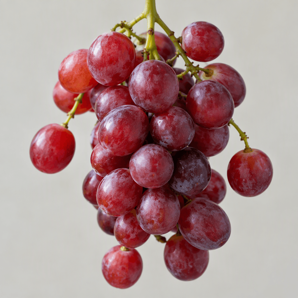 A cluster of round red grapes with smooth, slightly translucent skins ranging from ruby red to deep purplish red hangs from thin green stems, with a few grapes spaced loosely around the bunch.