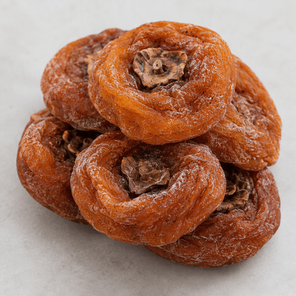 Whole dried persimmons are flattened, round to oval fruits with deep orange-brown, wrinkled leathery skin and occasional fine white sugar crystals on the surface.