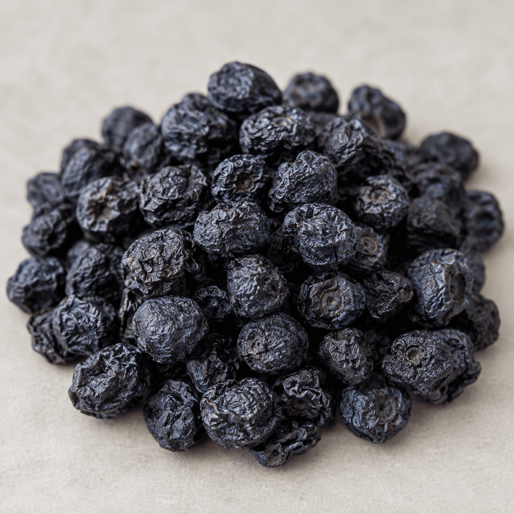 Small, round dried blueberries with wrinkled, slightly shriveled skins in deep blue-purple to nearly black tones, shown as a loose pile with a matte, leathery texture.