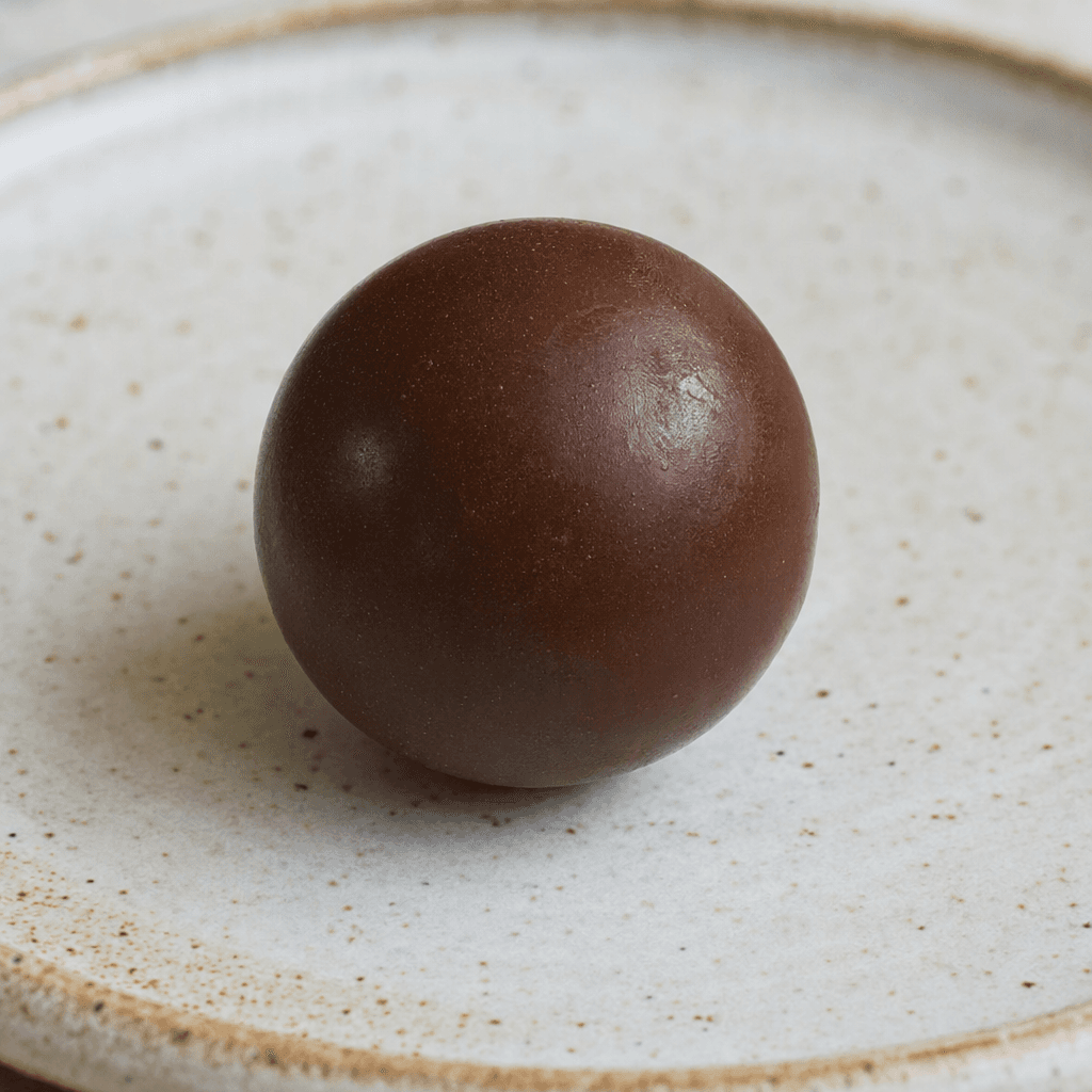 A small, round, dark-brown chocolate ball with a smooth, slightly glossy surface, served on a plate.