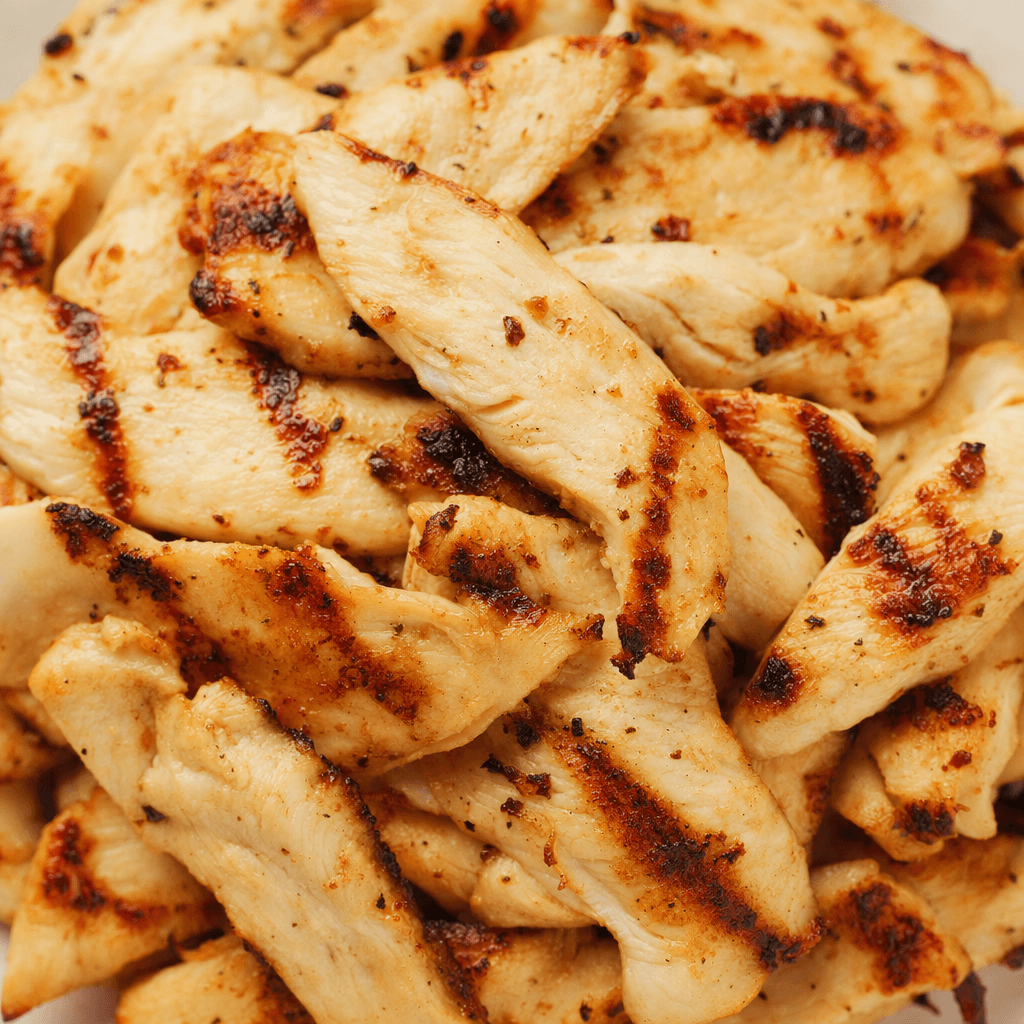 Thin, irregular slices of grilled chicken are piled together, with pale beige interiors and lightly browned edges marked by darker grill lines.