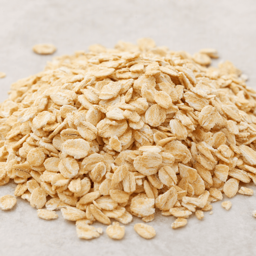 A small pile of raw oats made up of flat, narrow, pale beige flakes with slightly uneven edges and a dry, matte surface.