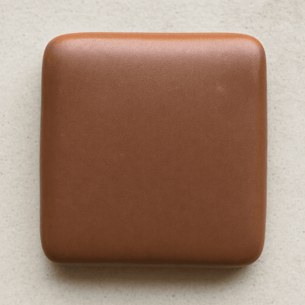 A small, flat square of milk chocolate with softly rounded corners and a smooth, lightly glossy brown surface.