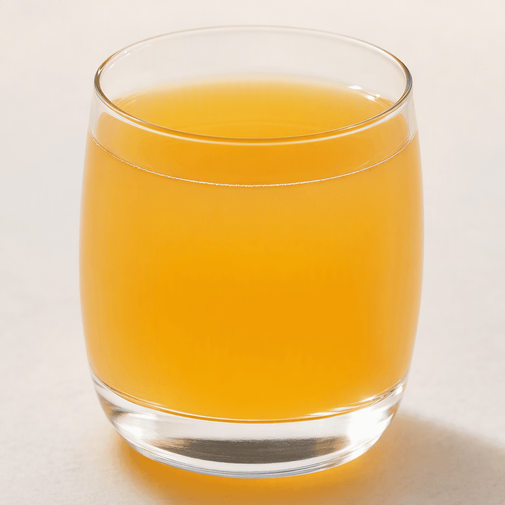 A translucent golden-orange drink fills a clear glass, with a smooth surface and no visible pieces of fruit.