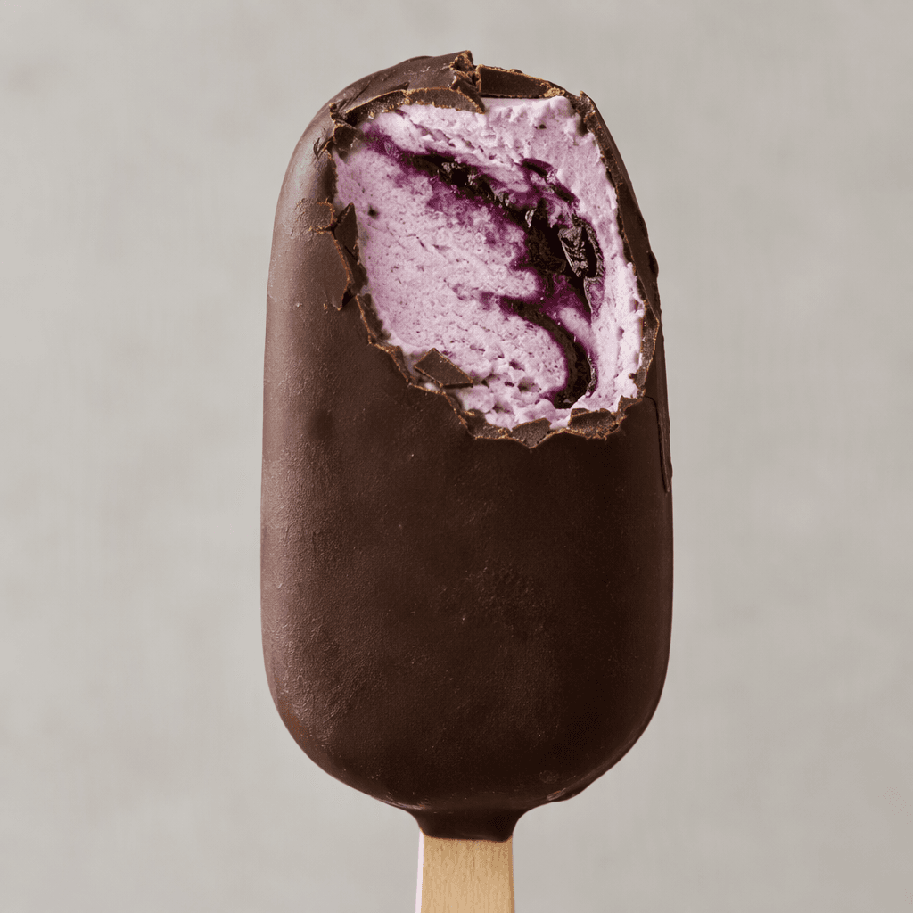 A thick, rounded rectangular ice-cream bar on a wooden stick, coated in dark chocolate, with a pale berry-purple ice-cream centre and a deep purple blackberry swirl visible in the cut surface.