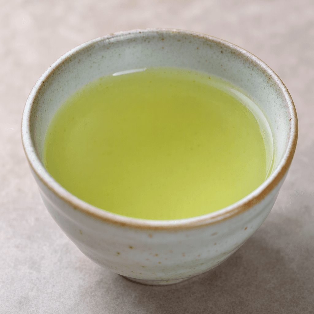 A clear, pale yellow-green tea sits in a small cup, with a faint green tint and no visible leaves or other ingredients.