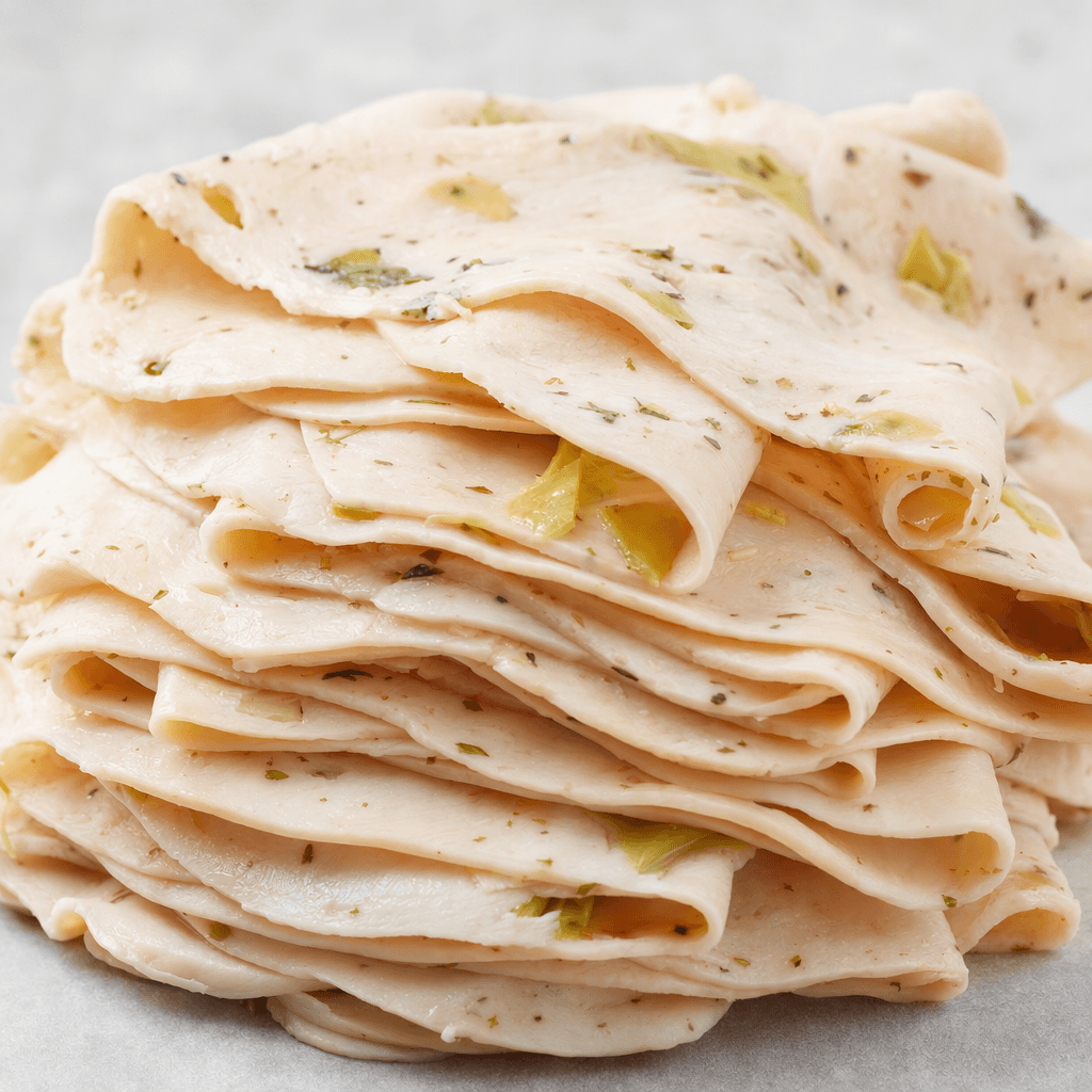 Thin, overlapping slices of pale pink turkey breast form a neat stack, with small green artichoke pieces and seasoning flecks visible throughout.