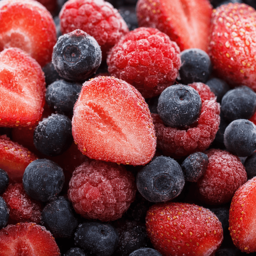 A loose mixture of whole and halved frozen berries, including deep red raspberries, dark blue-black blueberries, and glossy red strawberries, with a frosty coating and scattered ice crystals visible on their uneven, firm surfaces.