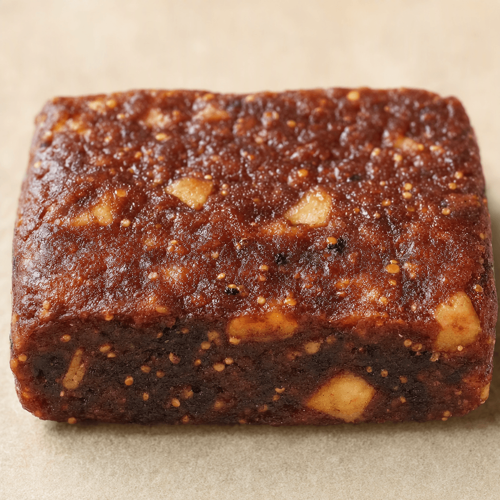 A compact rectangular fruit bar with a slightly uneven, dark reddish-brown surface, dotted with tiny fig seeds and occasional lighter apple pieces.