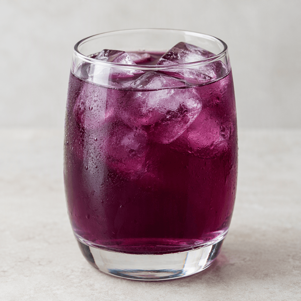 A deep purple, slightly translucent drink fills a clear glass, with ice cubes visible near the surface.