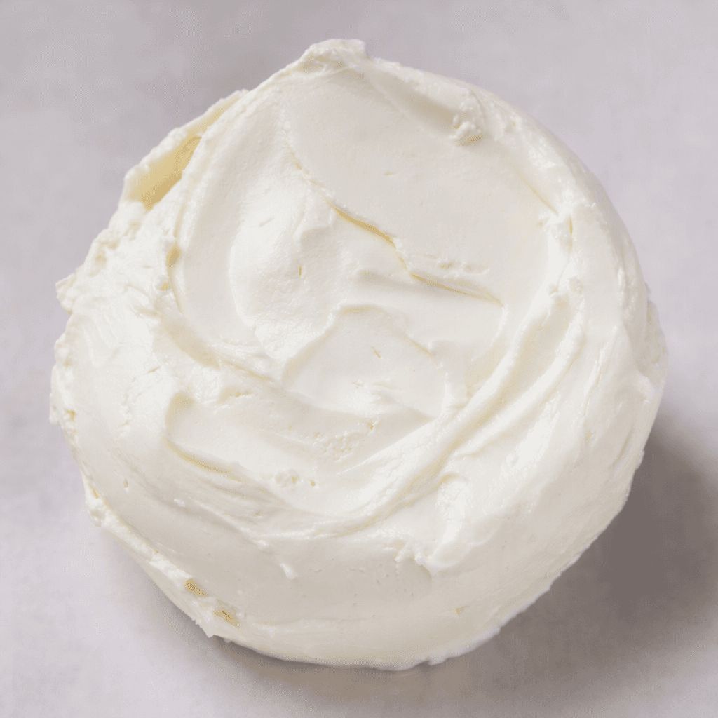 A soft, smooth, creamy-white cheese with a moist, thick consistency, shown in a rounded mound with gentle spreading marks.