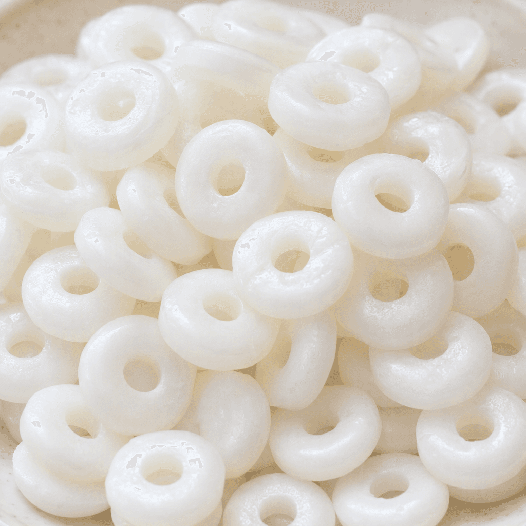Small, opaque white hard candies are arranged together, each a smooth, flat disc with a round hole through the centre and a faintly glossy surface.