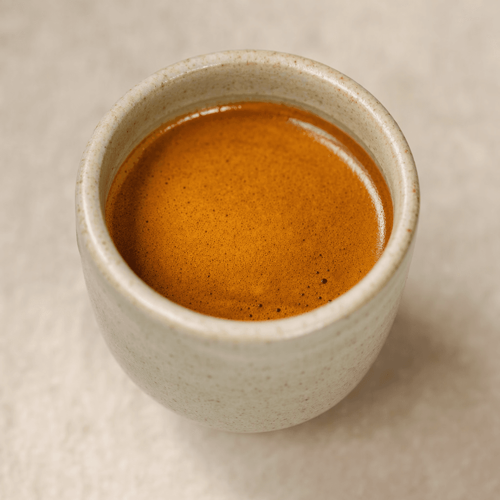 Küçük bir fincanda, yüzeyinde ince ve açık kahverengi köpük tabakası bulunan koyu renkli espresso.