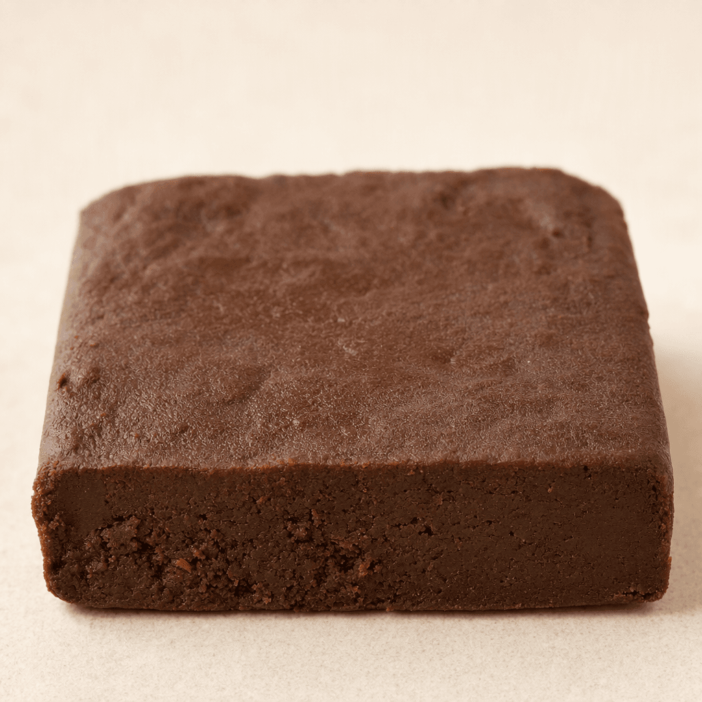 A compact rectangular cocoa-brown bar with a matte, slightly uneven surface and a dense, finely textured interior visible along one edge, served on its own.