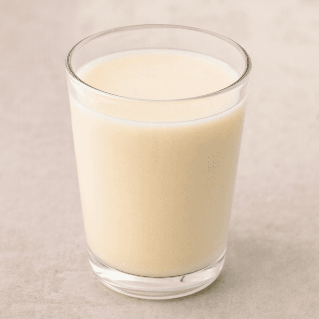 Berrak bir bardağı, pürüzsüz ve homojen dokulu, opak açık fildişi renkli hindistan cevizi içeceği dolduruyor.