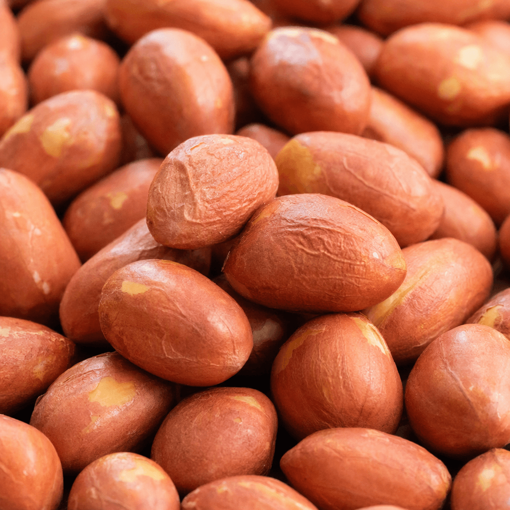 A small pile of oval peanut kernels with thin, wrinkled reddish-brown skins and golden-tan patches.