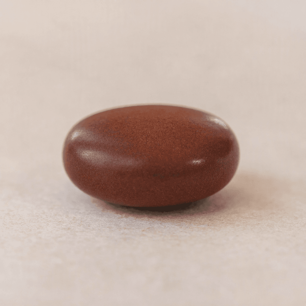 A small, smooth, dark reddish-brown tablet with a rounded shape rests by itself on a plain surface.