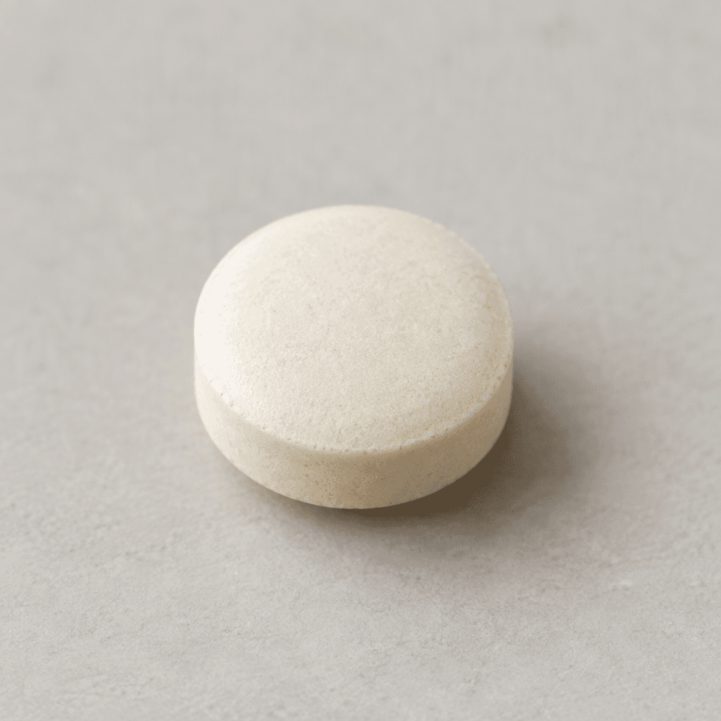A small, round, pale off-white tablet with a smooth, compact surface, shown on its own.
