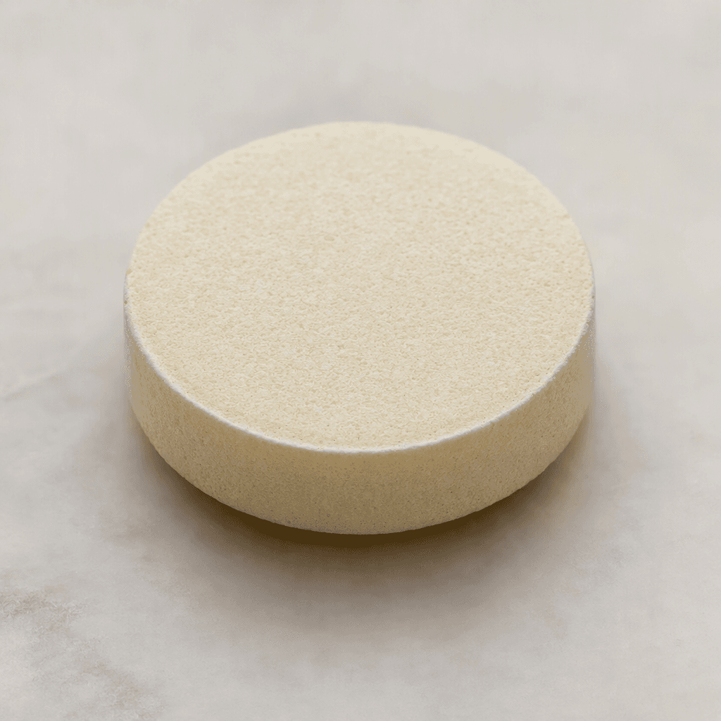 A pale cream, round effervescent tablet with a flat, lightly chalky surface and softly beveled edges.