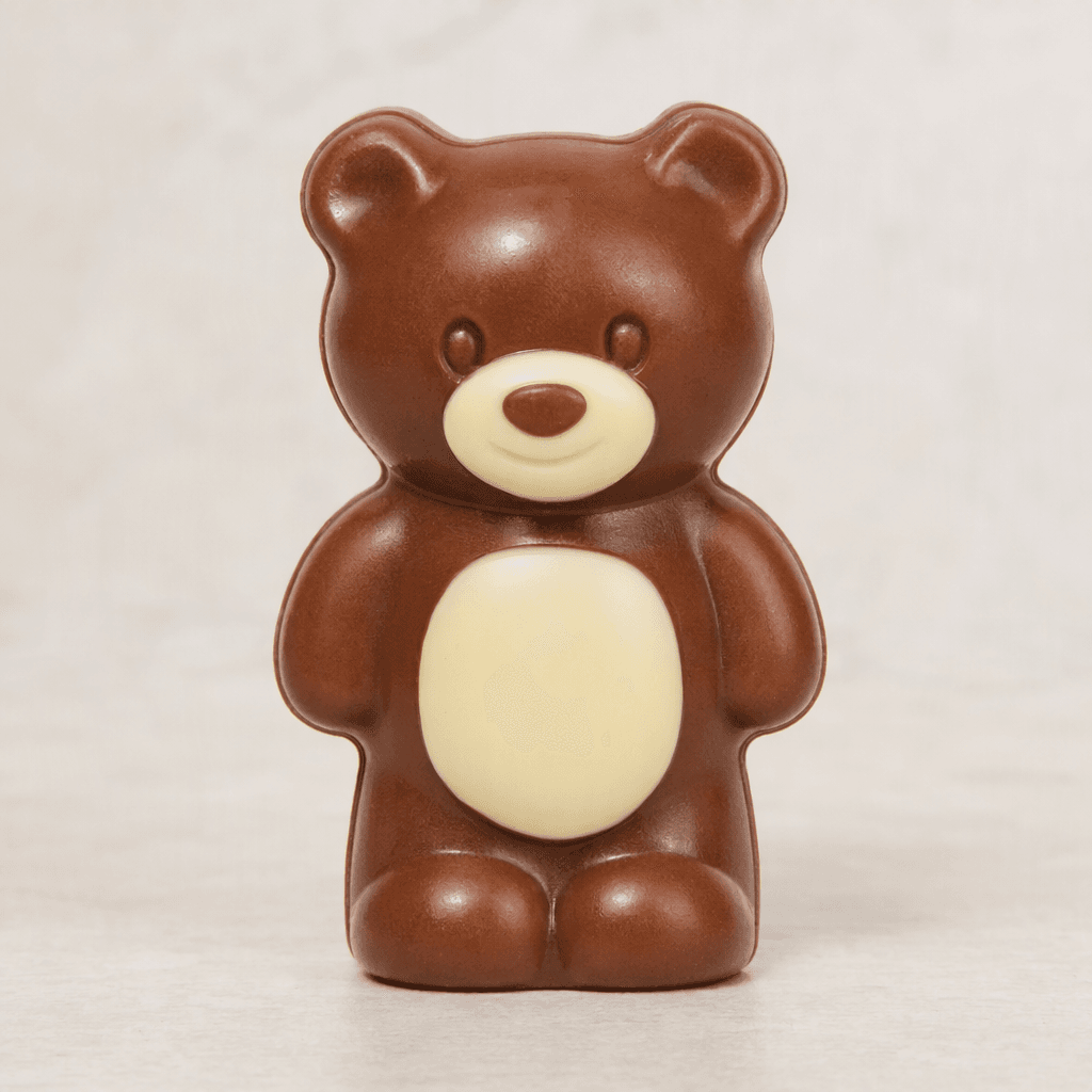 A small, glossy milk-chocolate bear shape with a pale white-chocolate muzzle and belly, shown by itself.