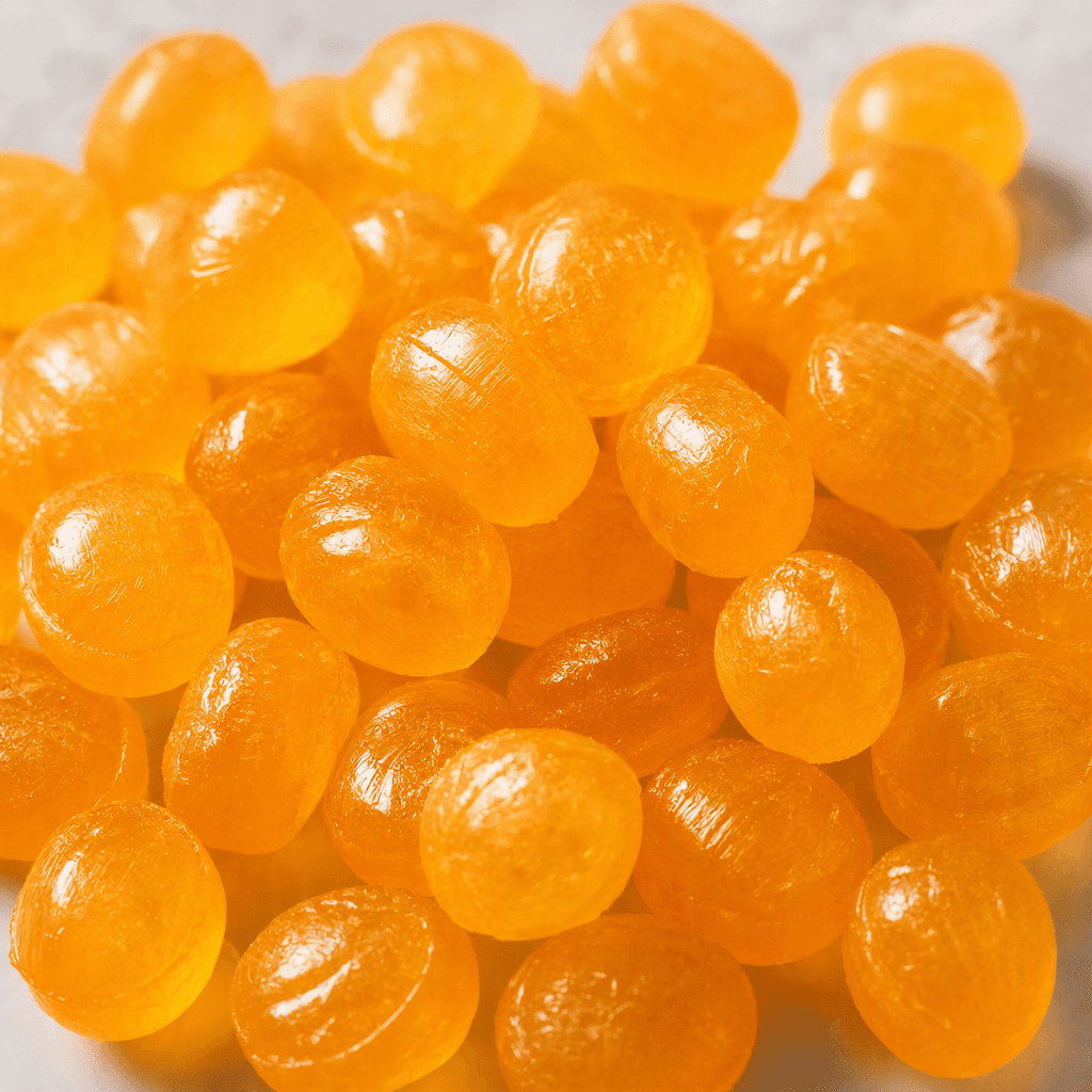 Small, glossy orange-yellow hard candies with smooth, rounded shapes are arranged in a loose pile.