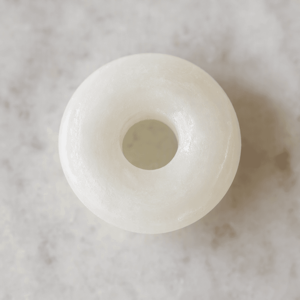 A small, white, hard candy shaped like a flat ring, with a round hole in the center and a smooth, slightly glossy surface.