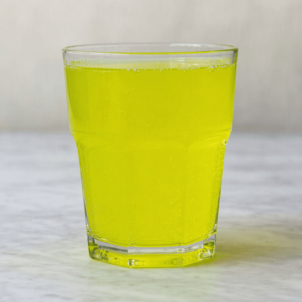 A translucent, bright yellow-green drink sits in a clear glass, with a smooth, even colour and a few small bubbles.