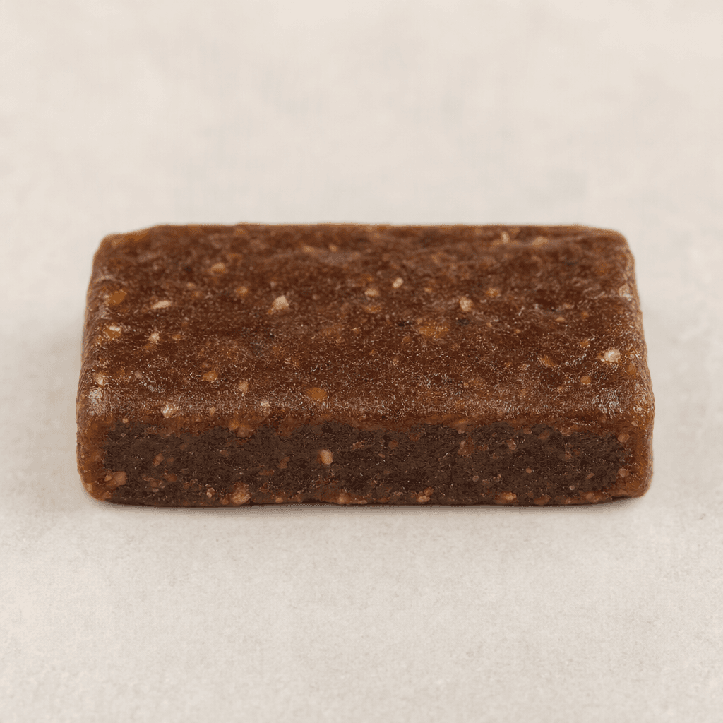 A compact, rectangular brown protein bar with a slightly uneven, dense-looking surface and softly rounded edges, shown on its own.