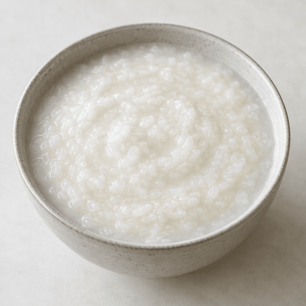 A bowl of thick, smooth, pale ivory rice porridge with a softly creamy surface and no visible toppings.